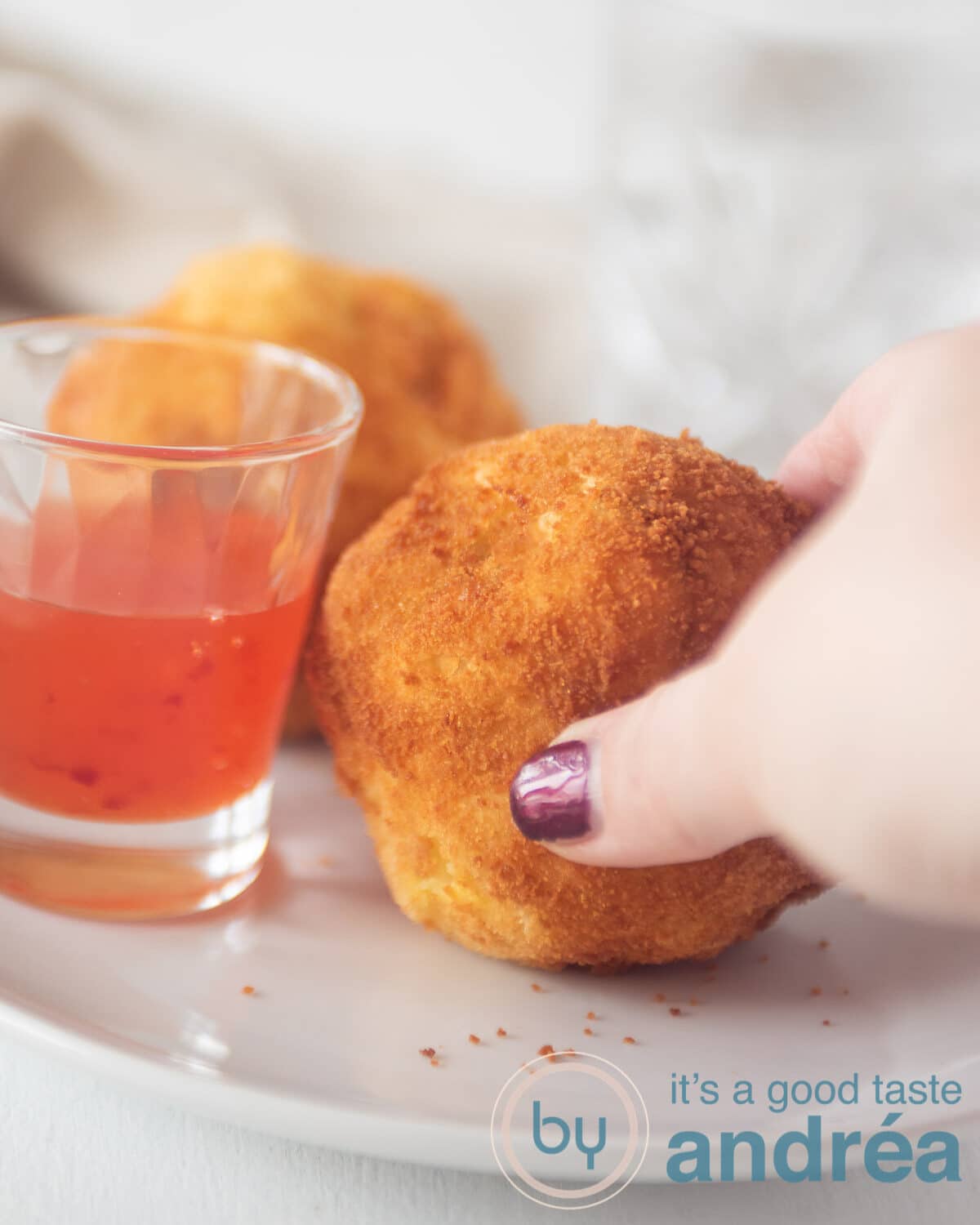 Een hand die een papas rellenas van de schaal pakt. Met een glaasje chilisaus