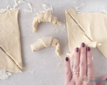 Een hand rolt croissants in vorm van deeg.