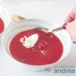 Vierkante uitsnede van een kom soep met Italiaanse tomatensoep met mascarpone. Een hand neemt een hap