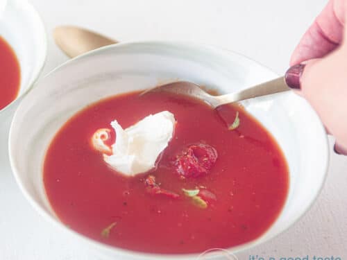 Vierkante uitsnede van een kom soep met Italiaanse tomatensoep met mascarpone. Een hand neemt een hap