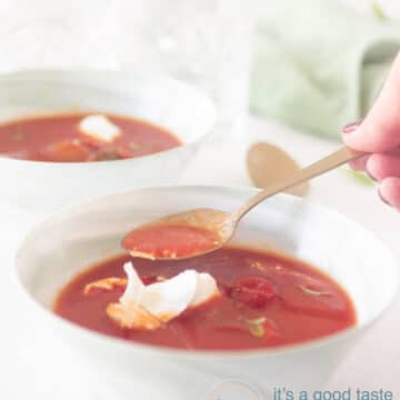 Italiaanse tomatensoep met mascarpone {met verse tomaten} twee groene kommen waar een lepel uit wordt gehaalt. Een witte ondergrond.