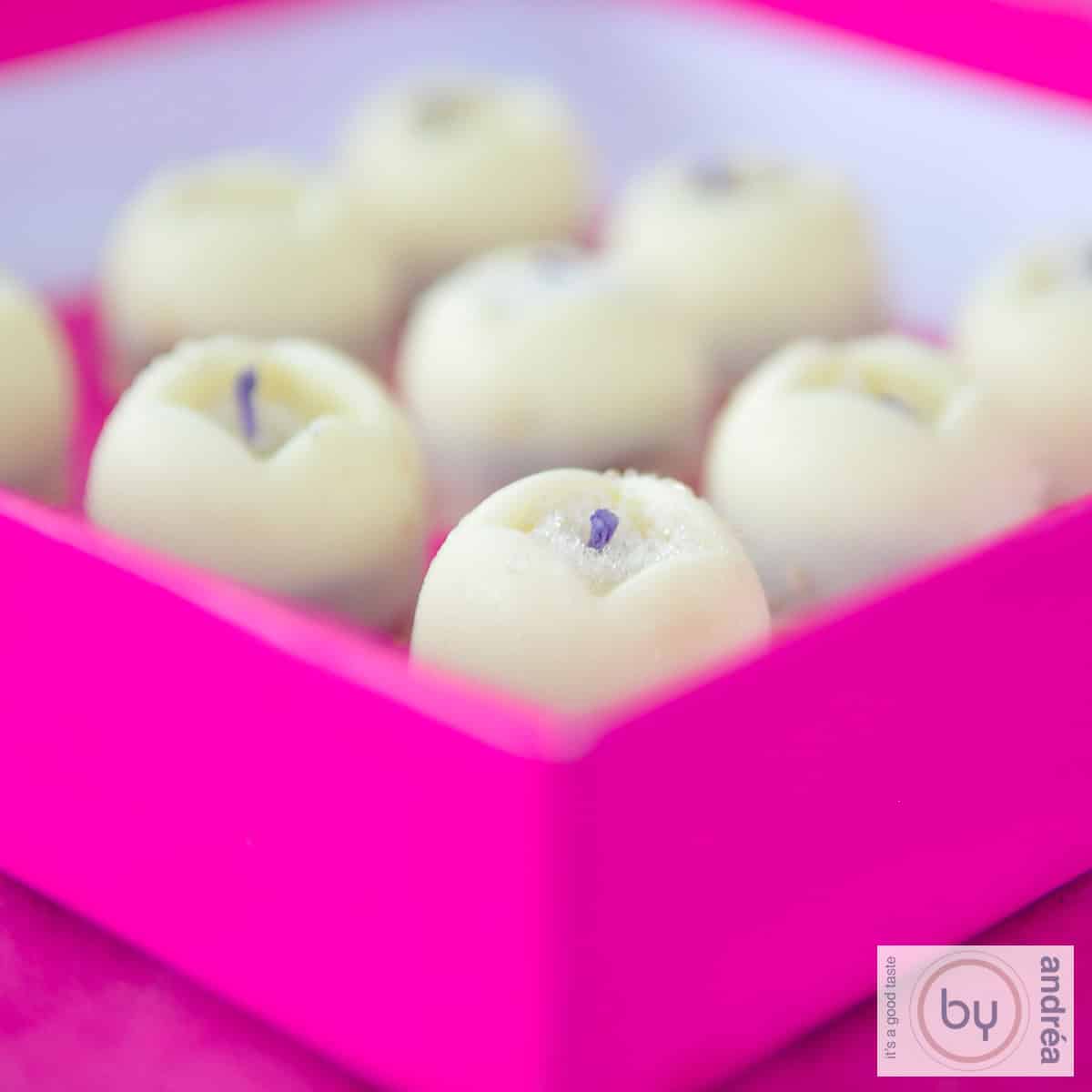 Een vierkante foto met een roze doos met witte chocolade lavendel bonbons erin.