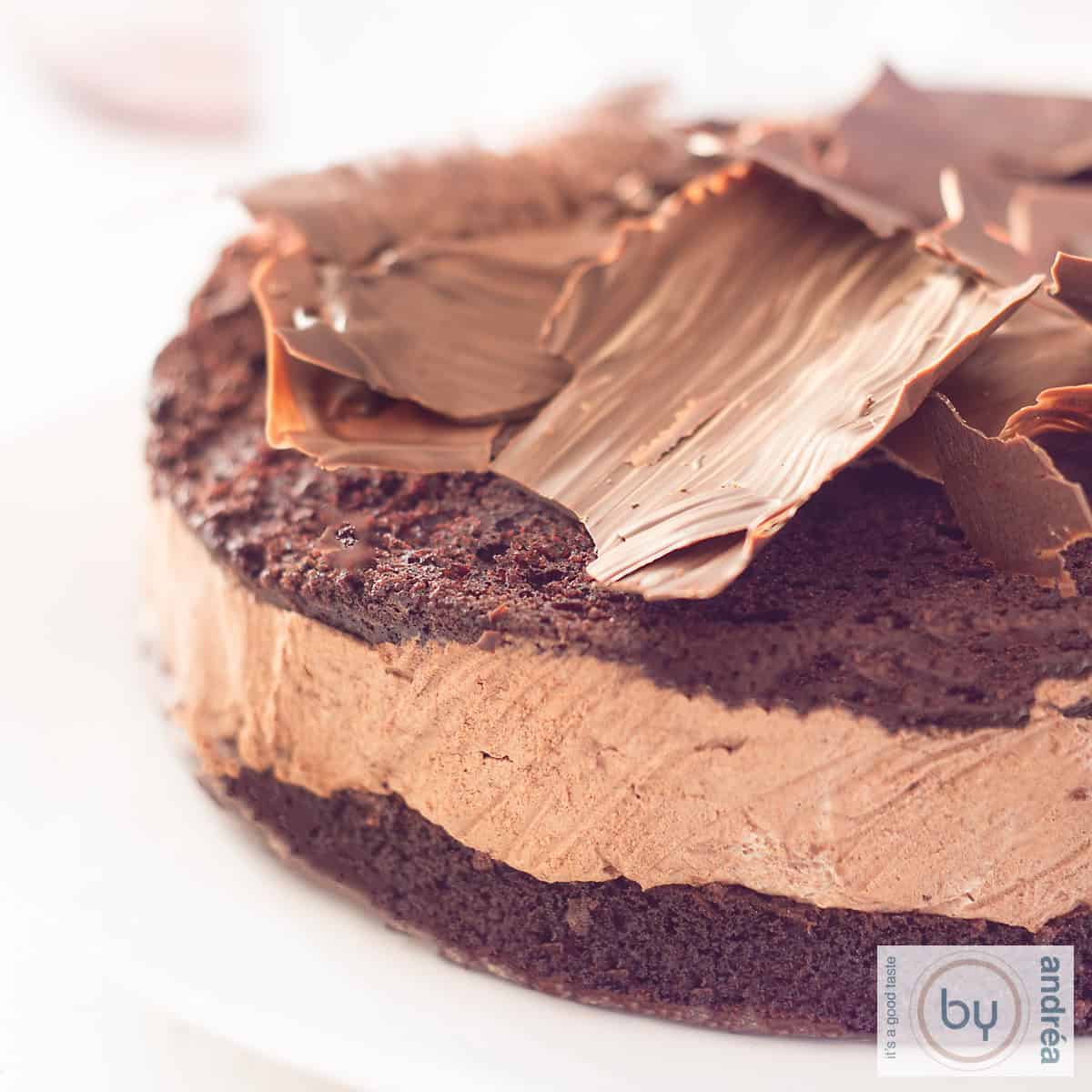 Een vierkante foto van een deel van een chocoladetaart met mousse en chocolade schilfers, zelfgemaakt, bovenop. Een witte achtergrond.