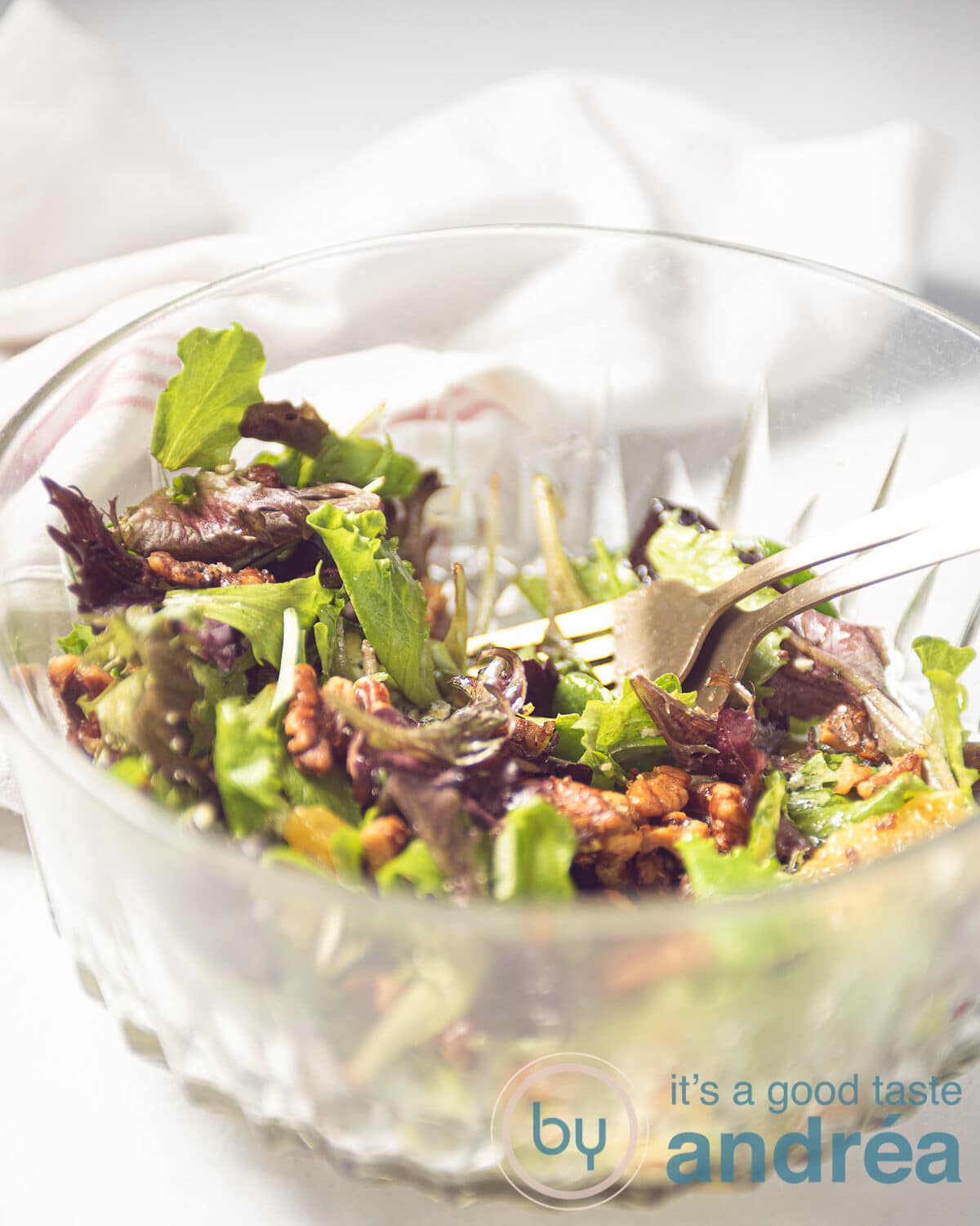 een glazen schaal met twee gouden vorken en een sinaasappel salade