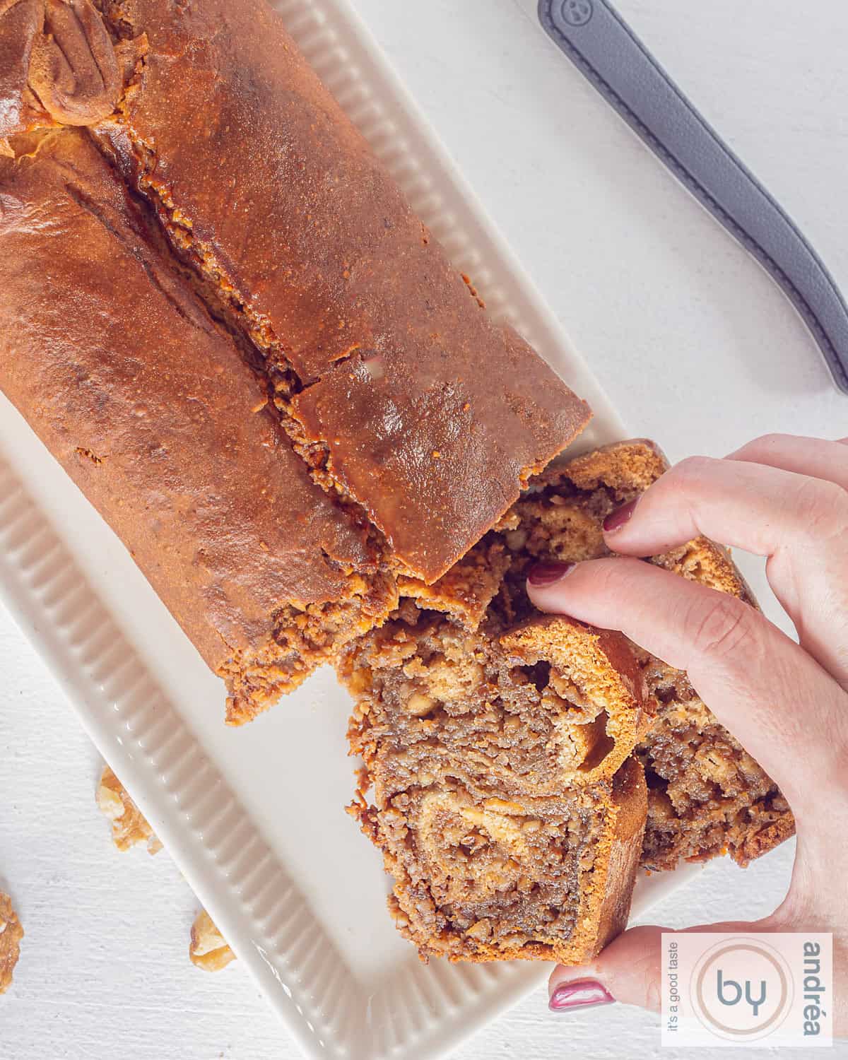 Een hoogtefoto van bovenaf genomen. Een walnotenbrood, povitica, waar twee plakjes afgesneden zijn. Een hand pakt een plakje.