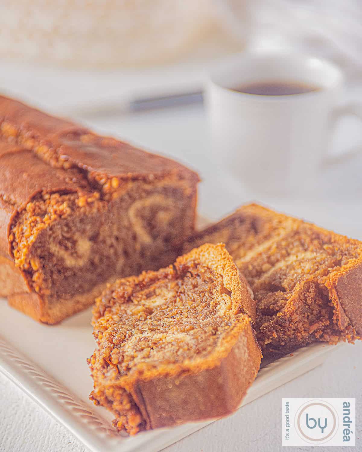 Foto van een povitica, een rijk gevuld walnotenbrood. Ervoor liggen twee afgesneden plakken zoet brood. In de achtergrond een kopje koffie.