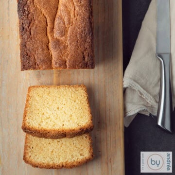 Een vierkante foto met een deel van een houten plank met een cake waar twee plakjes afgesneden zijn en ervoor liggen. Aan de rechterkant ligt een mes.