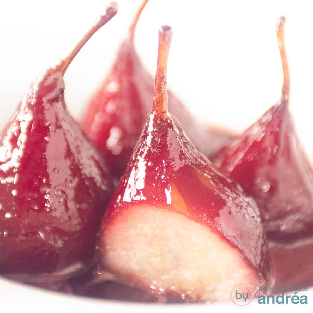 Four poached pears on a white plate. One pear is a slice cut off.