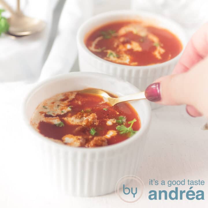 Een vierkante foto met twee kommen met een soep van tomaten, room en peterselie