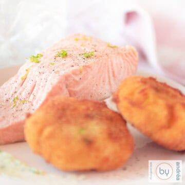 Een vierkante foto met twee wasabi aardappel kroketjes en gerookte zalm, warm, gemarineerd op een wit bord.