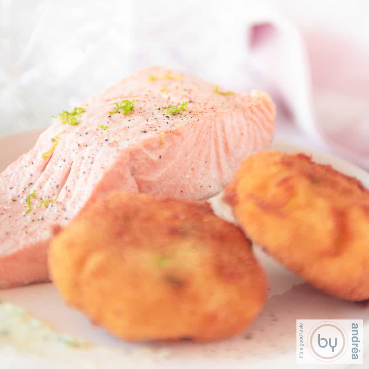 Een vierkante foto met twee wasabi aardappel kroketjes en gerookte zalm, warm, gemarineerd op een wit bord.