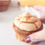 Een vierkante foto met een cupcake met karamel creme en karamelsaus. Een hand pakt de cupcake