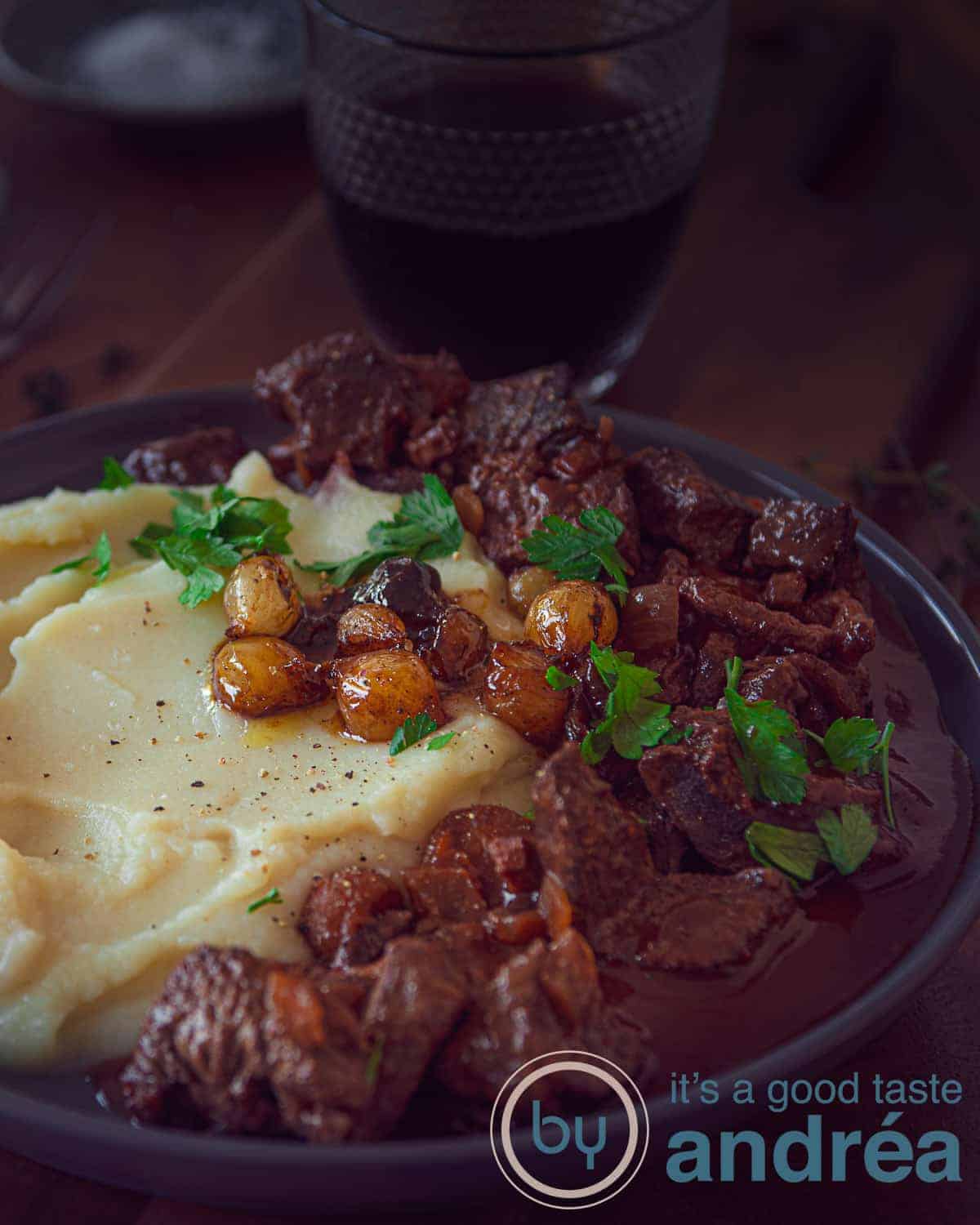 Een foto met een bord met aardappelpuree, boeuf bourguignon en gekarameliseerde uitjes op een donkere achtergrond