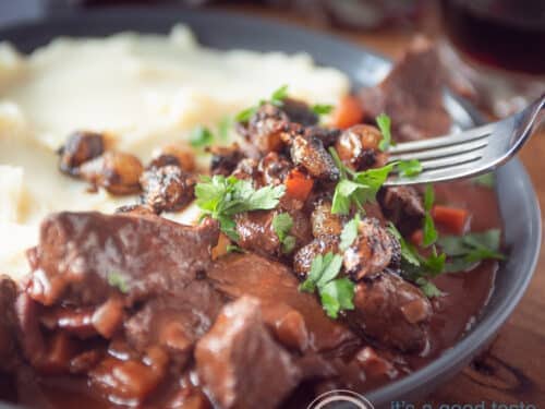 Een vierkante foto met een grijs bord, aardappelpuree, franse boeuf bourguignon met peterselie.