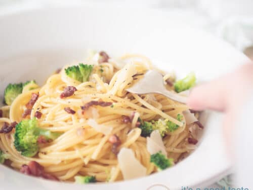 Een vierkante foto met een bord spaghetti, een hand die er wat uitpakt en brocolli, spekjes en Parmezaanse kaas