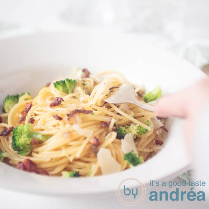 Een vierkante foto met een bord spaghetti, een hand die er wat uitpakt en brocolli, spekjes en Parmezaanse kaas