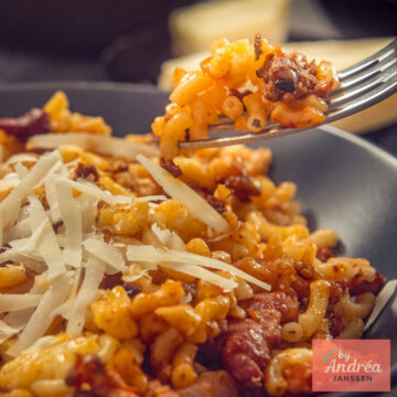 Vork met macaroni en gehakt boven een bord macaroni met spekjes en geschaafde Parmezaanse kaas.