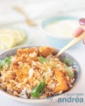 Blauwe Schaal met Kip Biryani. Een vork neemt een hand. Schijfjes citroen en raita op de achtergrond