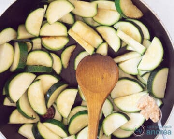 Aan een koekenpan met courgette schijfjes wordt knoflook toegevoegd.