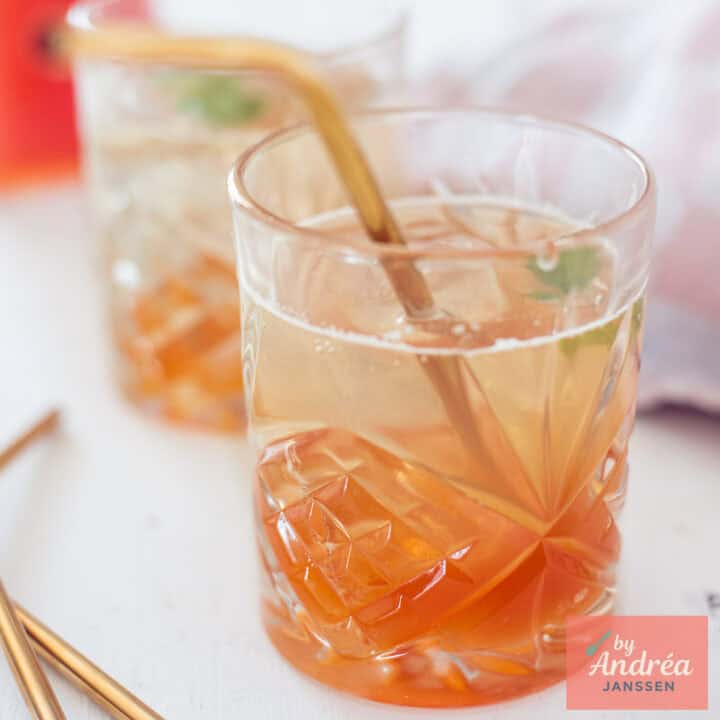 Een vierkante foto met twee glazen met rozenbottelsiroop aangelengd met water In een glas.