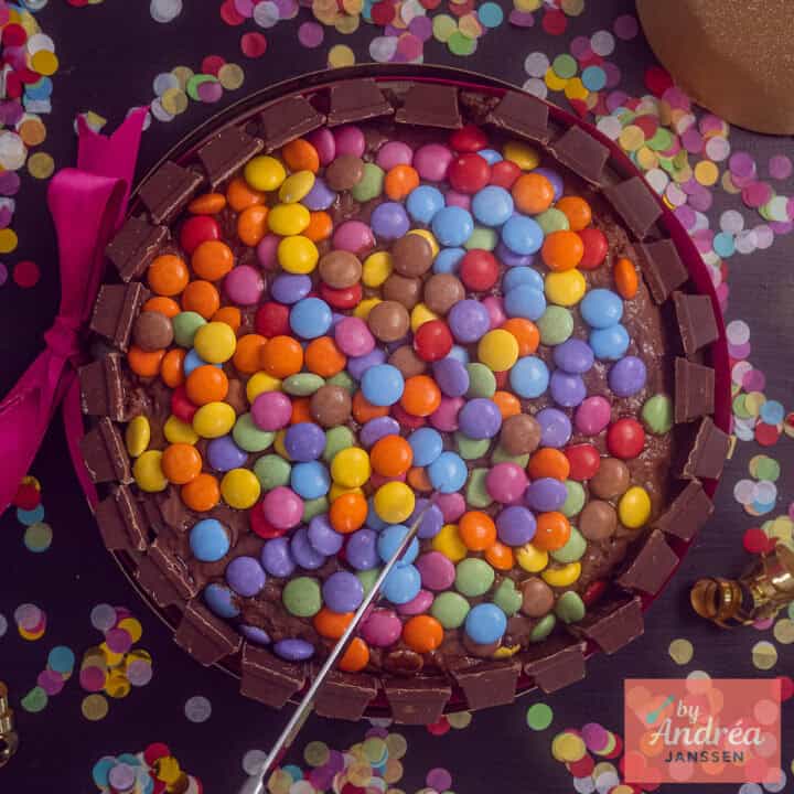 Een vierkante foto met een Kitkat taart met smarties en confetti eromheen.