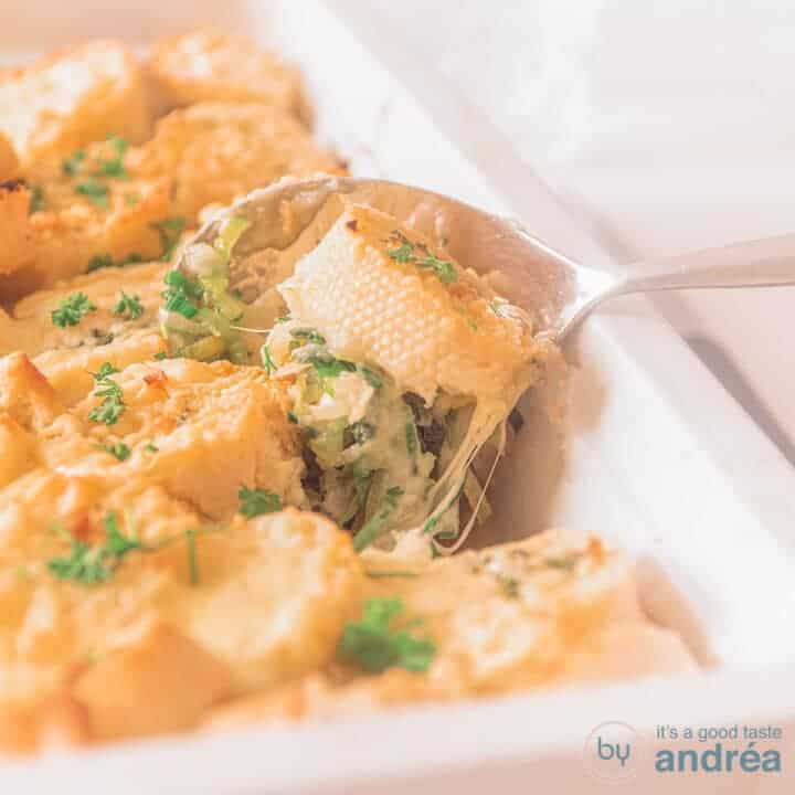 Een vierkante foto met een witte ovenschaal. Een schep kip prei en een stokbrood worden eruitgeschept. Gegratineerde kaas.