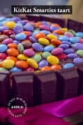 Een deel van een Kitkat smarties taart met een roze strik. Een tekst: uitkat smarties taart