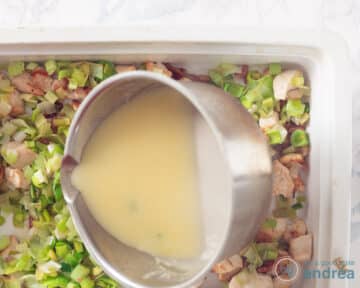 De saus wordt over de kip prei gegoten in een witte ovenschaal.