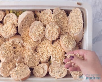 Een witte ovenschaal bedekt met plakjes stokbrood waar geraspte kaas over wordt gestrooid.