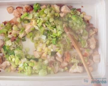 Een witte ovenschaal met een mengsel van aangebakken kip en gesmoorde prei.