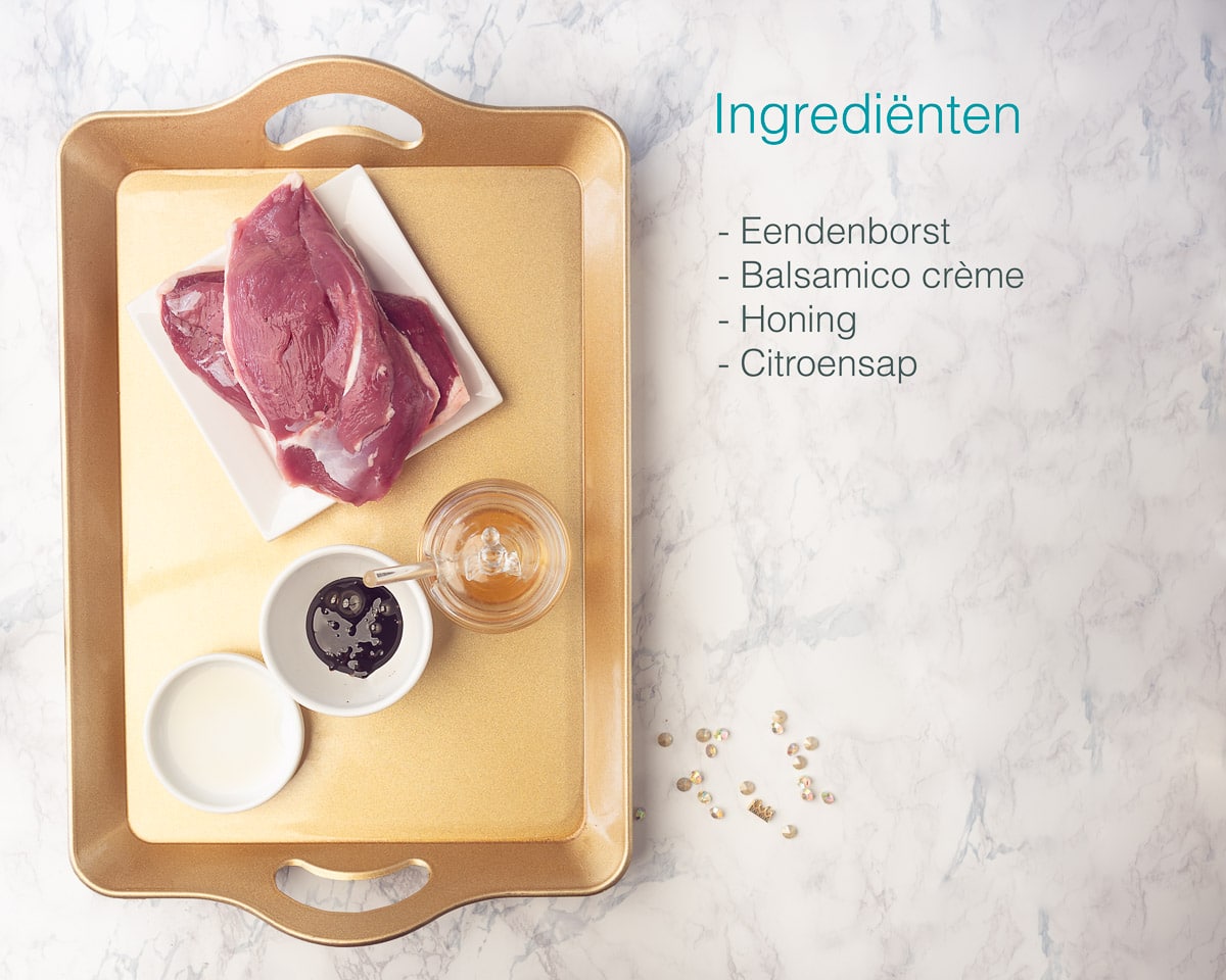 Ingrediënten Eendenborst met Honing Balsamico Saus op een gouden dienblad met een marmeren ondergrond. Een tekst met alle ingredienten