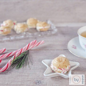 Een vierkante fotomet een wit kerstschaaltje met een macaron. Zuurstokken en een glazen schaal met extra macarons in de achtergrond