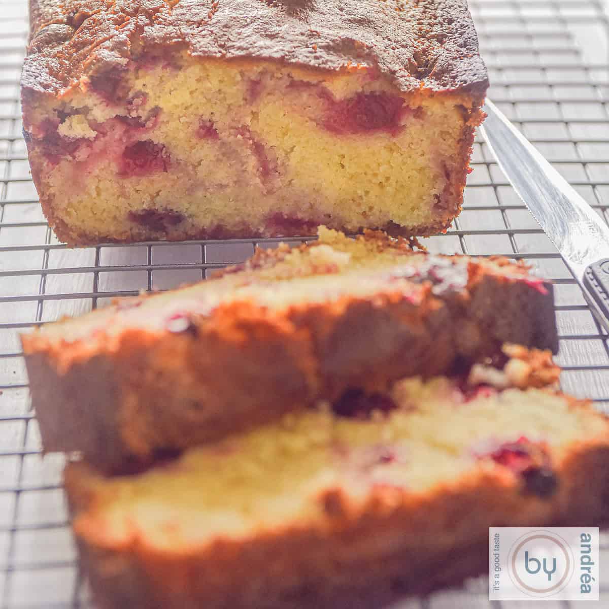 Een vierkante foto met een cake waar twee plakjes af zijn gesneden gevuld met cranberry's