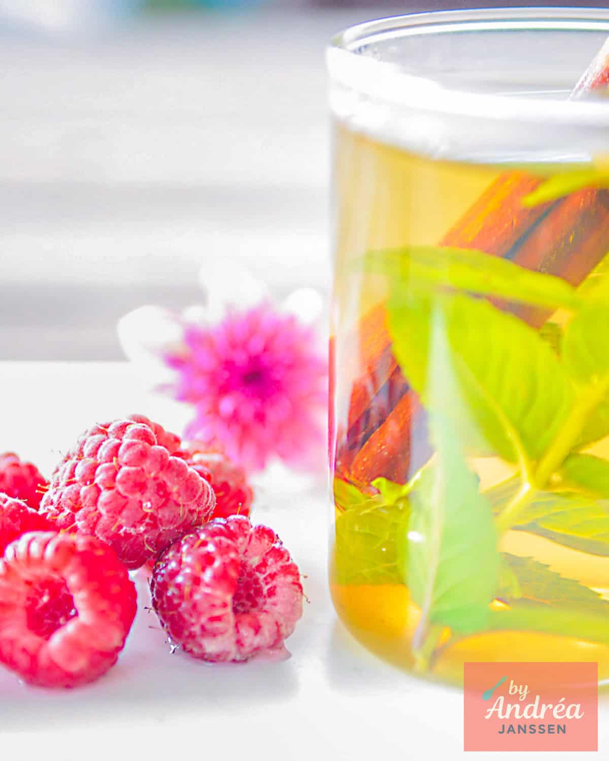 Part of a glass filled with tea with cinnamon, mint and lemon balm. Some raspberries on the side.