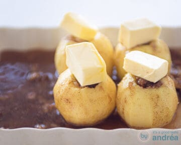 Gevulde appels op een bedje van rozijnen met een klont boter op de appels in een witte ovenschaal