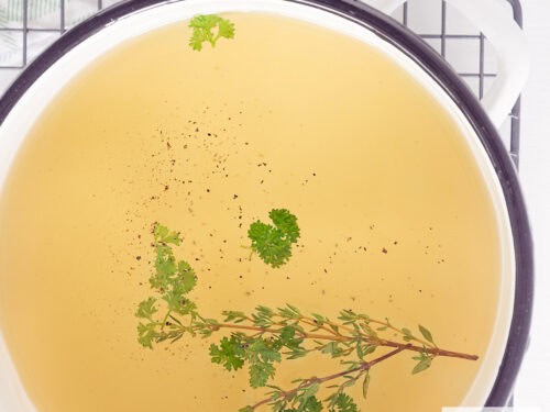 Een vierkante foto van een deel van een soeppan met groentebouillon met kruiden.