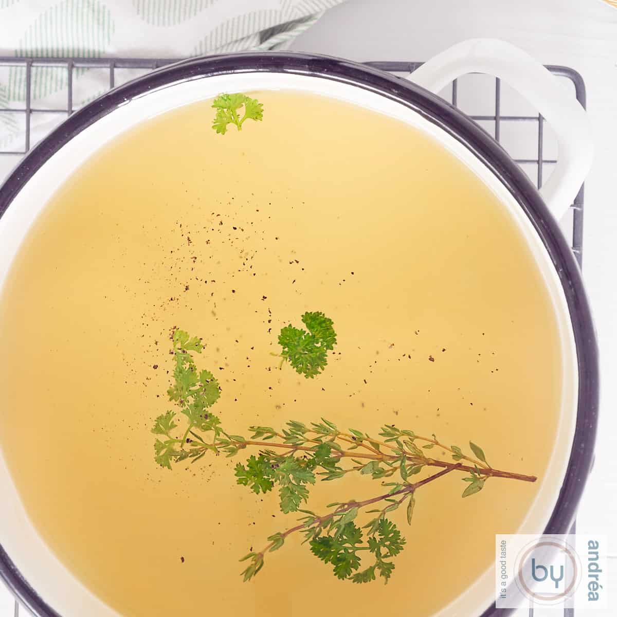 Een vierkante foto van een deel van een soeppan met groentebouillon met kruiden.