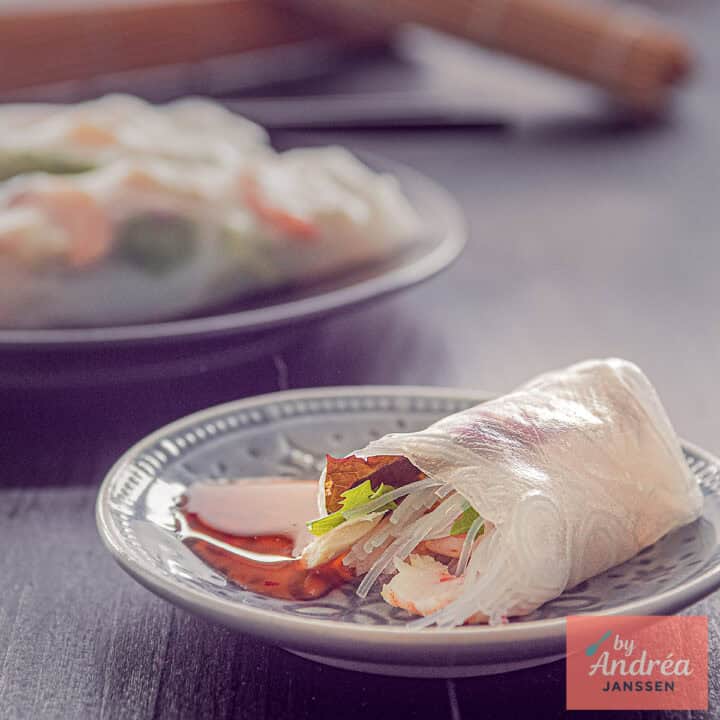 Een vierkante foto met een grijs bord met een rijstvel gevuld met salade, kip, garnalen en vermicelli