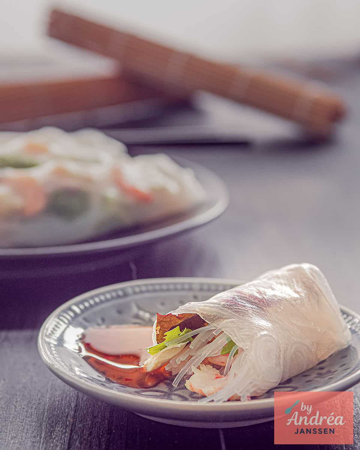 Een grijs bord in de voorgrond met een springrol gevuld met garnalen, kip, sla en vermicelli. Meer springrolls in de achtergrond.