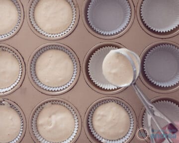 Papieren vormpjes in een cupcake vorm waar met een ijsschep beslag in wordt geschept. Sommige vormpjes zijn al gevuld.