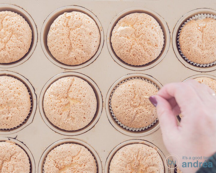 Een cupcake vorm met cupcakes waarin met een satéprikker gaatjes wordt geprikt
