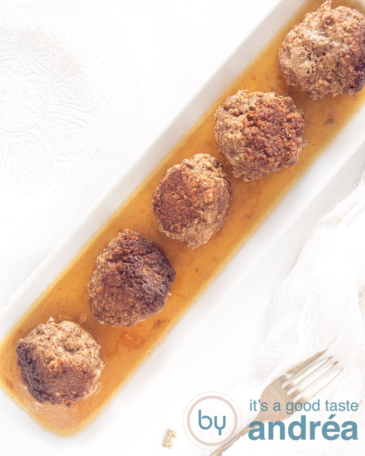 foto bovenaf 5 gehaktballen in de jus op een rijtje