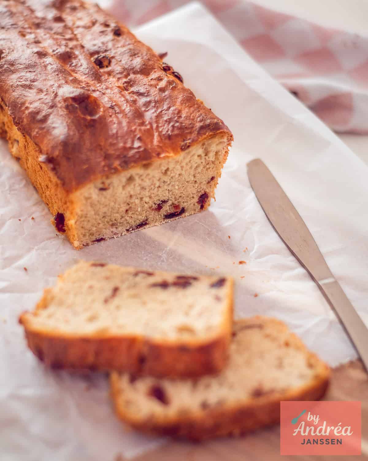 Cranberrybrood op een wit bakpapier met twee sneetjes ervoor.