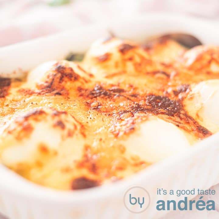 Een vierkante foto met een witte ovenschaal gevuld met gegratineerde eieren op een bedje van spinazie.