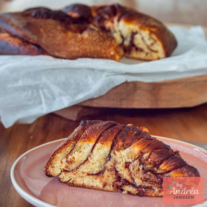 Een vierkante foto met een Nutella brood waar een partje uit is gesneden dat in de voorgrond ligt.