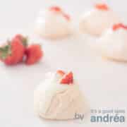 Een vierkante foto met rozen meringue op de voorgrond en drie in de achtergrond. Links aardbeien.