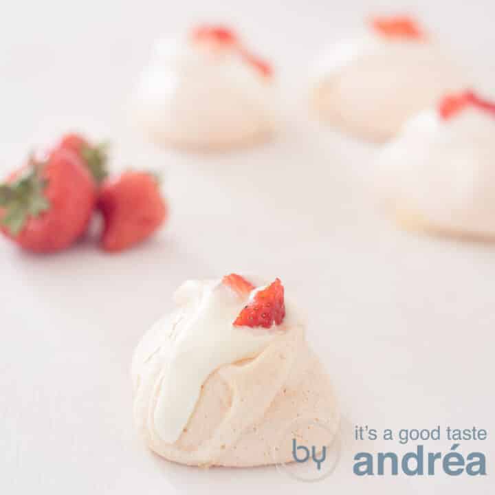 Een vierkante foto met rozen meringue op de voorgrond en drie in de achtergrond. Links aardbeien.