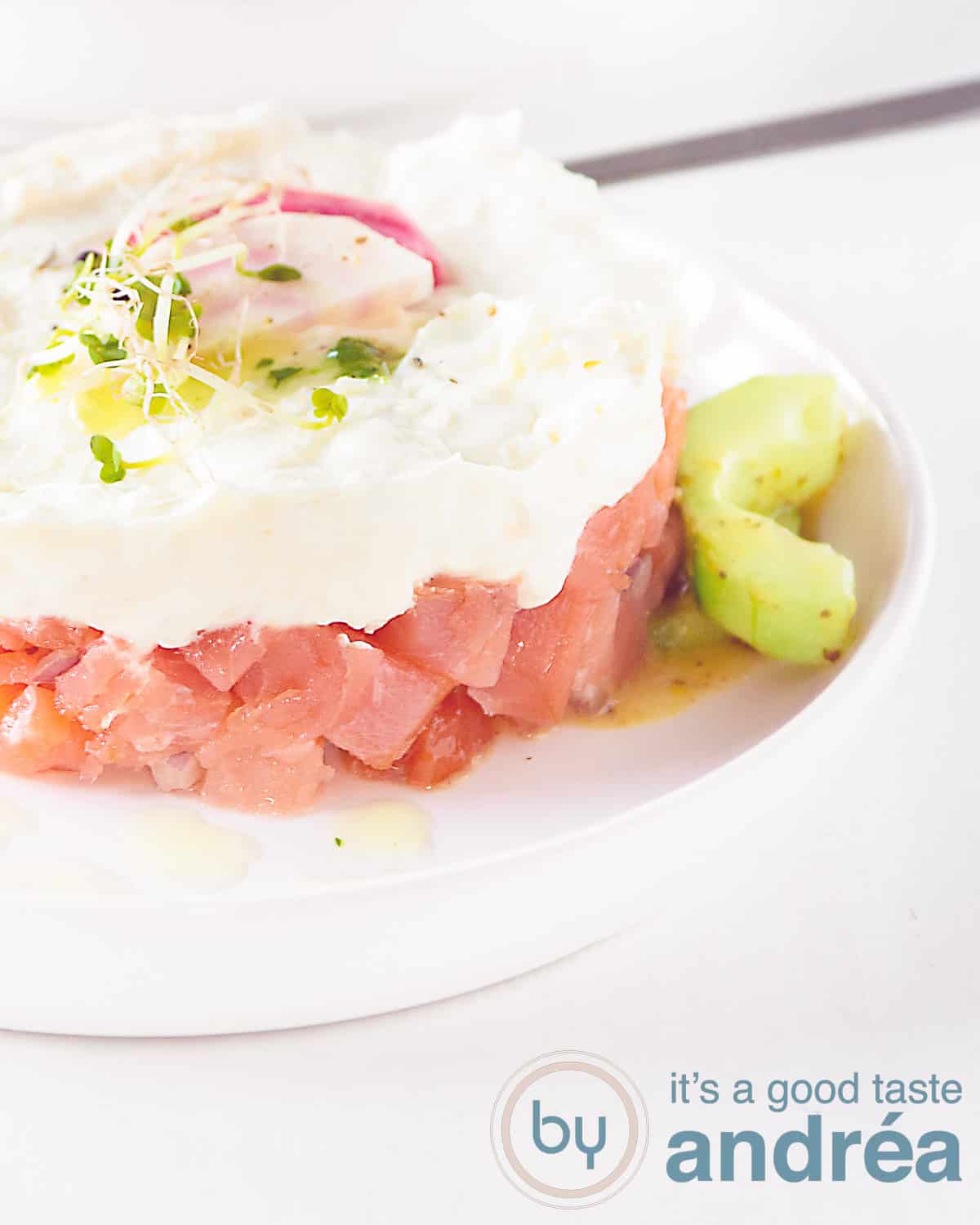 Een deel van een torentje met zalmtartaar en geitenkaas mousse met honing mosterd komkommer op een wit bord op een witte achtergrond