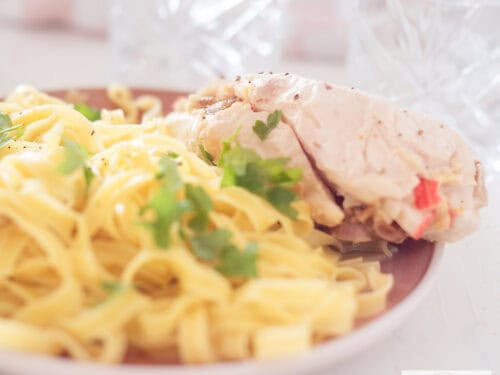 Een vierkante foto met een roze bord met tagliatelle en gevulde kip met dadels en surimi