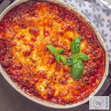 Een vierkante foto van een deel van een ovenschaal gevuld met lasagne met bolognesesaus en gesmolten kaas